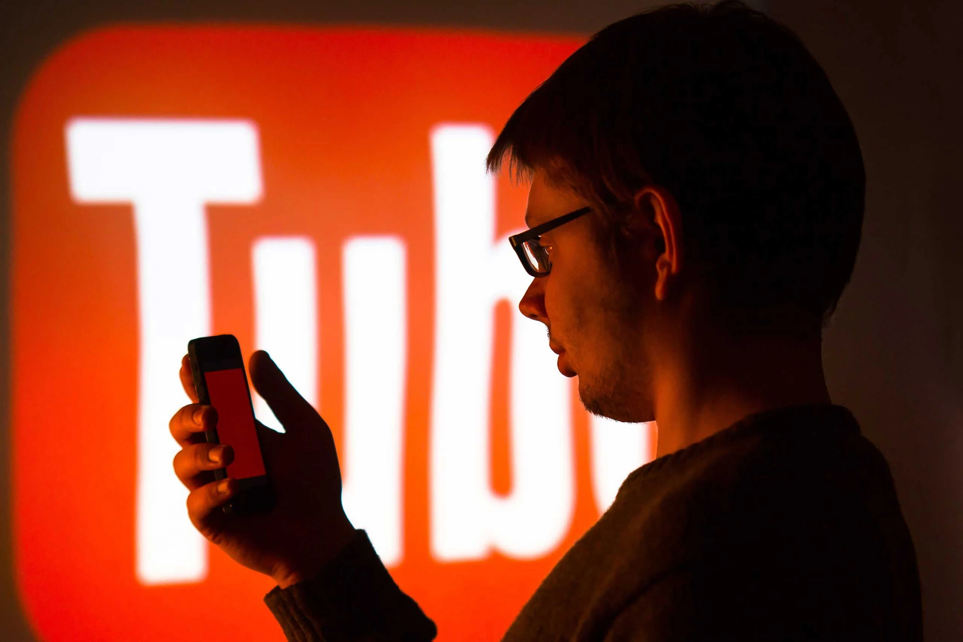 Person viewing a smartphone in front of a YouTube screen, representing video marketing, social media strategy, and mobile content.