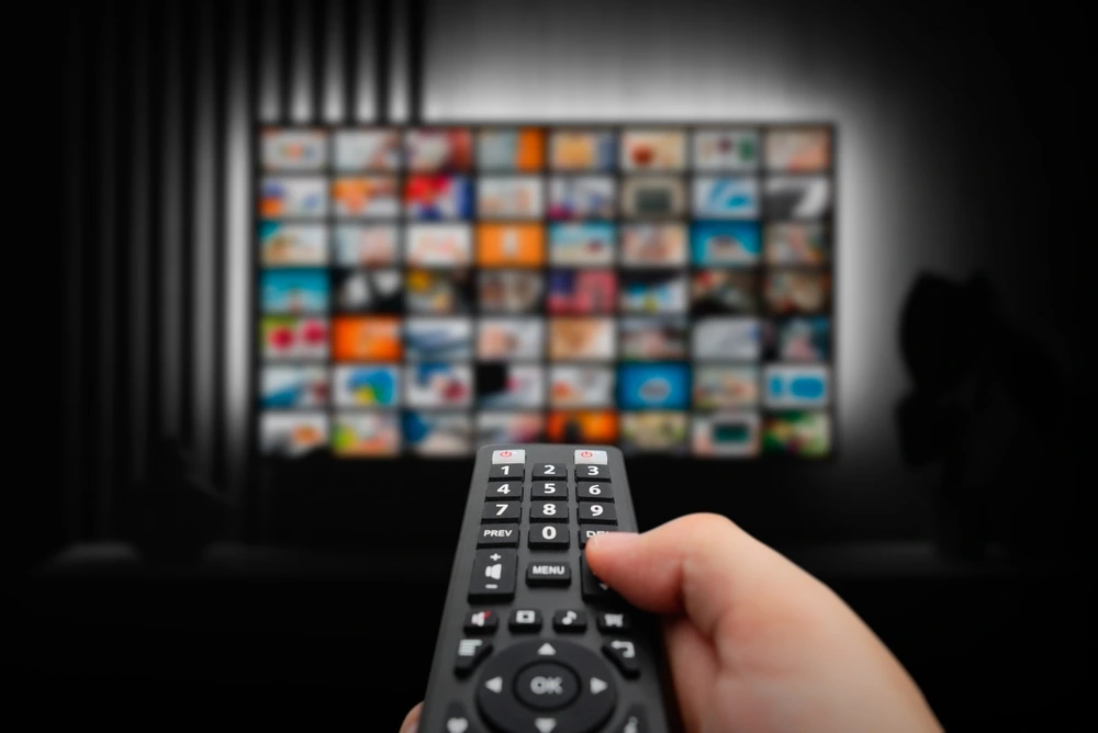 Hand using a TV remote to browse streaming content, representing OTT and CTV advertising for digital campaigns.