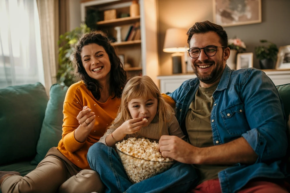 Smiling family sitting on a couch with a bowl of popcorn, representing home entertainment and connected viewing.